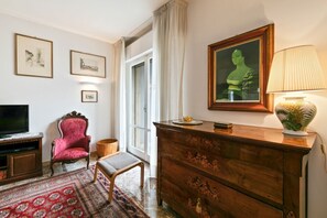 A room with a television, a red armchair, a wooden dresser, a patterned rug, and framed artwork on the walls.