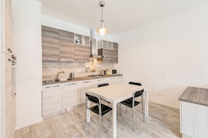 Una cocina moderna con comedor, que cuenta con armarios de madera clara, electrodomésticos de acero inoxidable y una lámpara colgante.