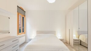 Un dormitori amb llit, taules de nit, un aparador, una finestra i un armari.