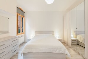 Un dormitorio con cama, mesitas de noche, cómoda, ventana y armario.