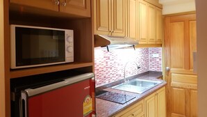Eine Küche mit Holzschränken, einer Mikrowelle, einem roten Kühlschrank und einer gefliesten Spritzschutzwand.
