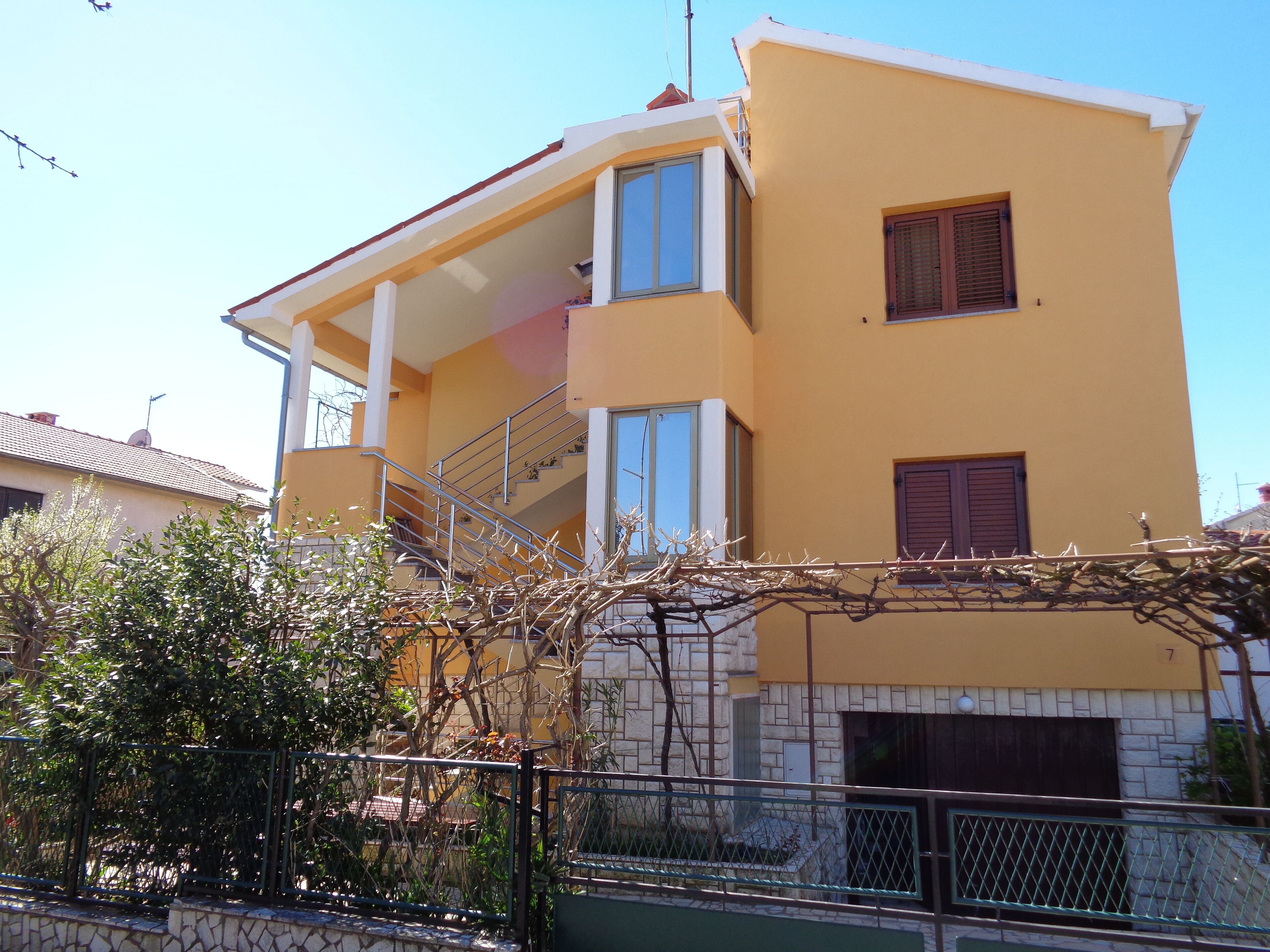 A two-story building with a yellow facade, a balcony, and a staircase leading to the upper floor.