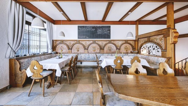Um restaurante com mesas e cadeiras de madeira, um menu em lousa e uma parede decorativa.