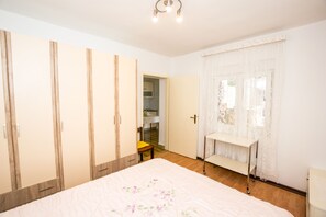 Quarto com uma cama grande, guarda-roupa de madeira, uma mesinha e uma cadeira.