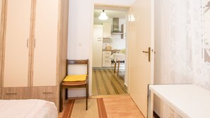 Une chambre à coucher avec un lit, une armoire en bois, une chaise avec un coussin jaune et une petite table.