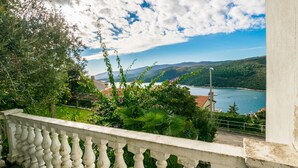 Un balcon doté d’une balustrade blanche, qui offre une vue sur un paysage côtier verdoyant et sur la mer.