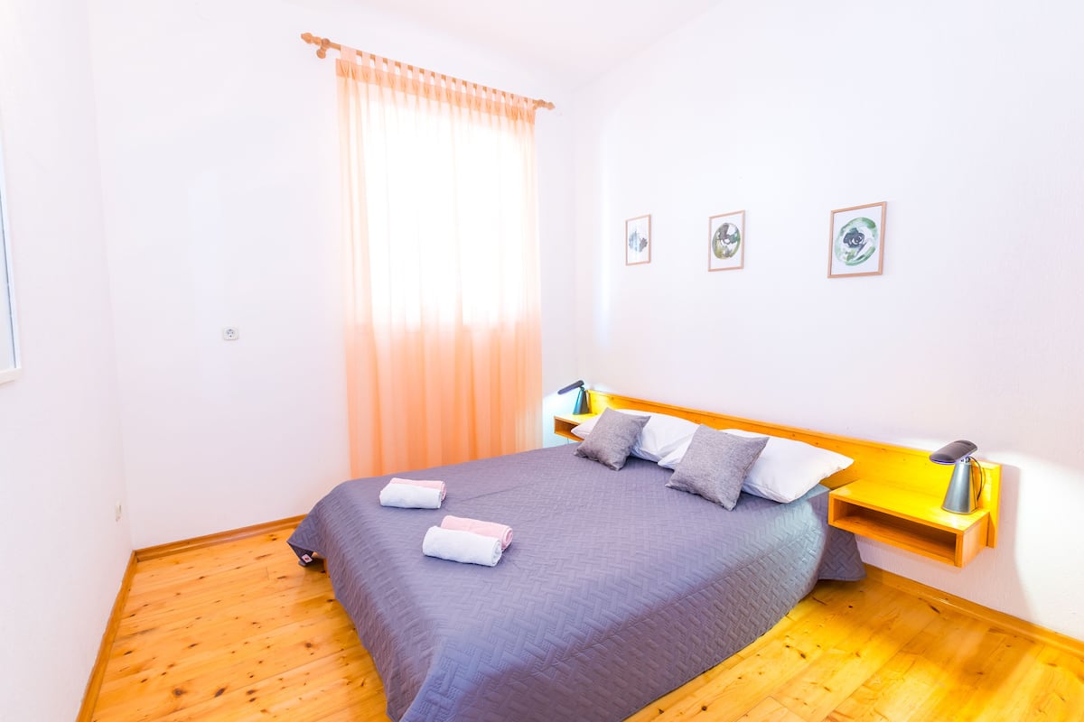 A neatly made bed with a headboard, a bedside table with a lamp, and three framed pictures on the wall.