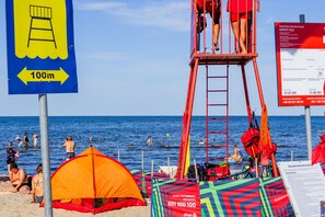 A beach with a lifeguard tower, tents, and a sign indicating a 100m distance. - SeaSide Sopot (Sopot)