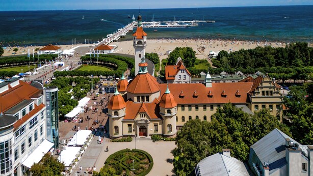 A historic building with a central tower, a waterfront promenade, and a beach with people. - SeaSide Sopot (Sopot)