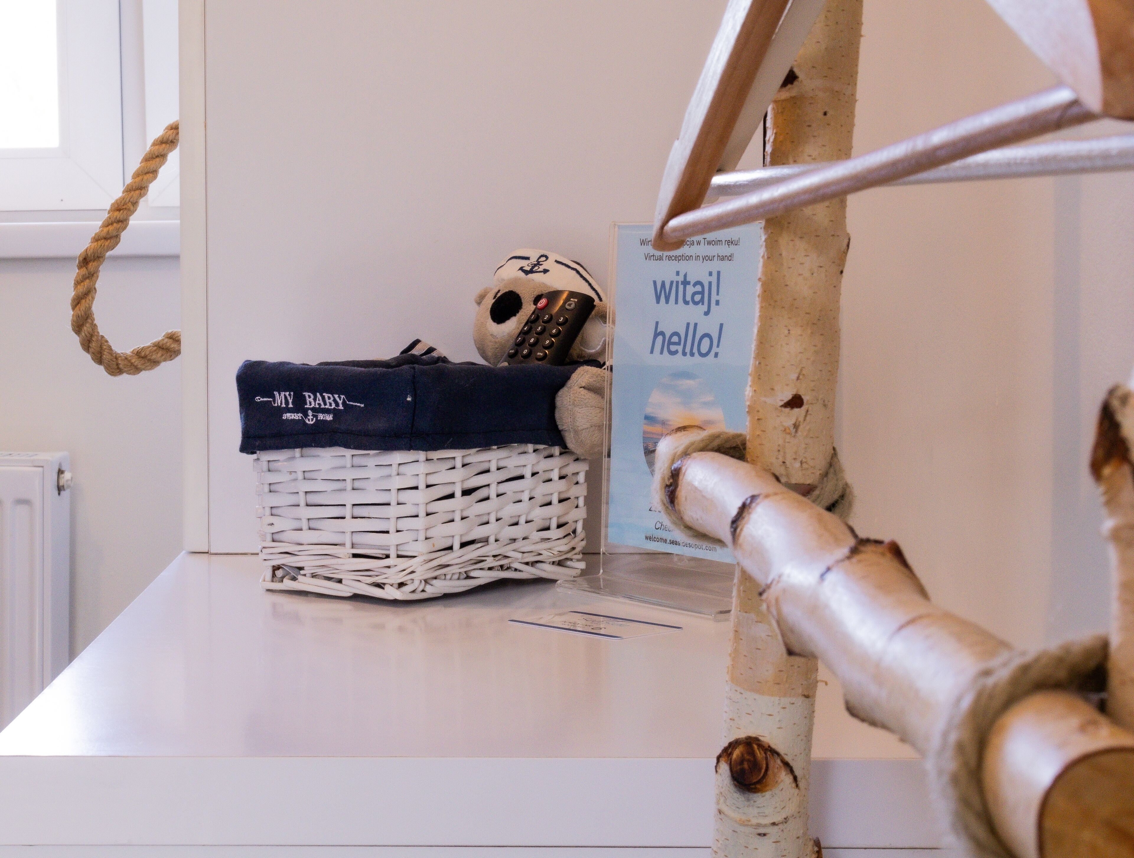 A room with a white table, a white basket with a dark cloth, a stuffed toy, and a sign with text.