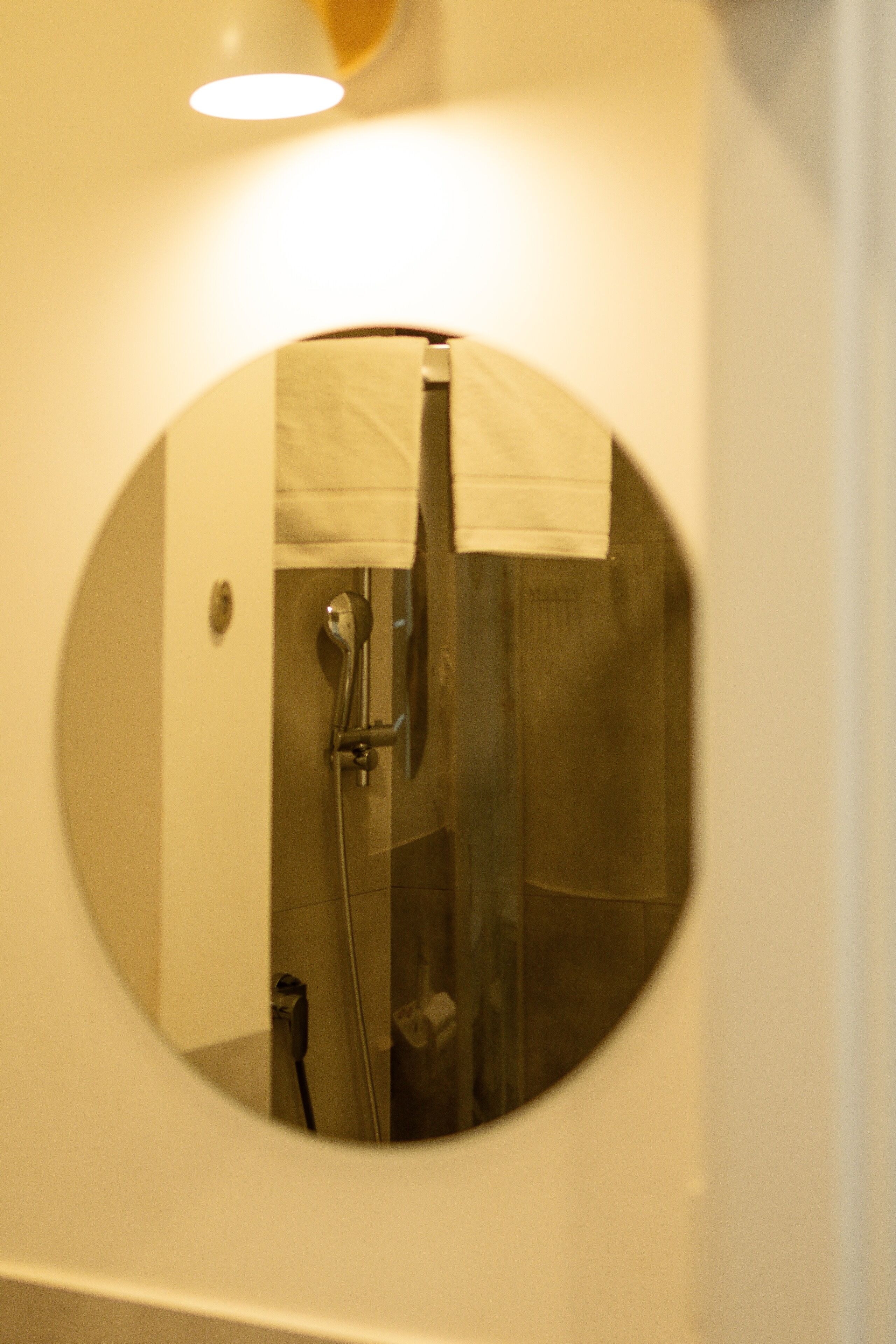 A circular mirror reflecting a shower area with a towel hanging on the wall.