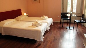 A hotel room with two beds, a small table with chairs, and a window with a view of greenery. - B&B Elio's Place (Seveso)