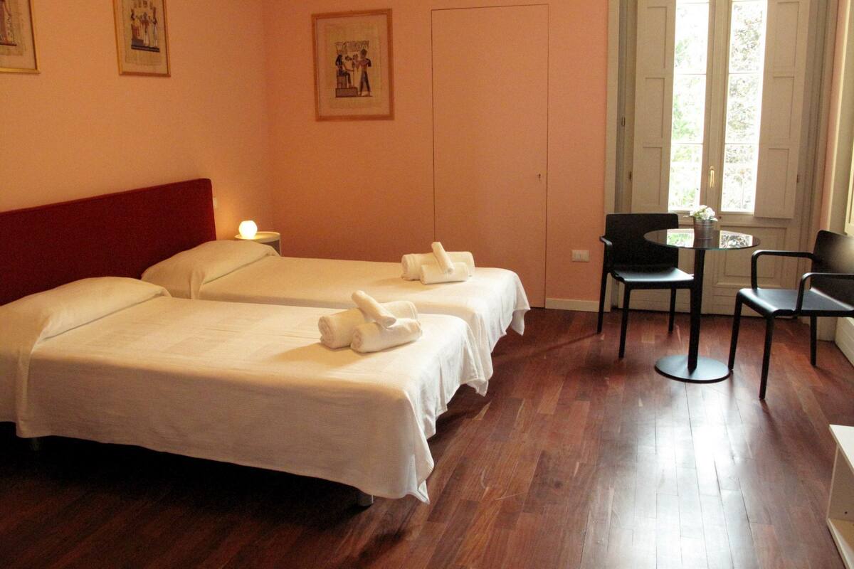 Ein Hotelzimmer mit zwei Betten, einem kleinen Tisch mit Stühlen und einem Fenster mit Blick ins Grüne.
