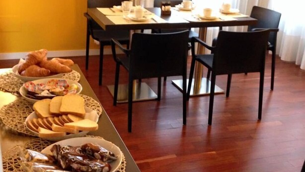 A breakfast buffet with croissants, bread, cheese, and pastries on a table, with a dining area featuring chairs and a table in the background. - B&B Elio's Place (Seveso)