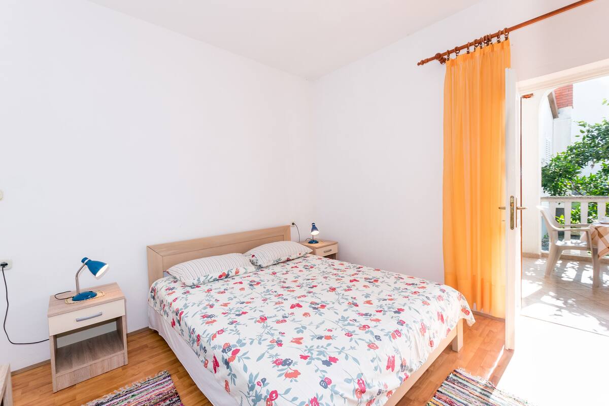 A bedroom with a wooden bed, a nightstand with a lamp, and a view of an outdoor balcony.
