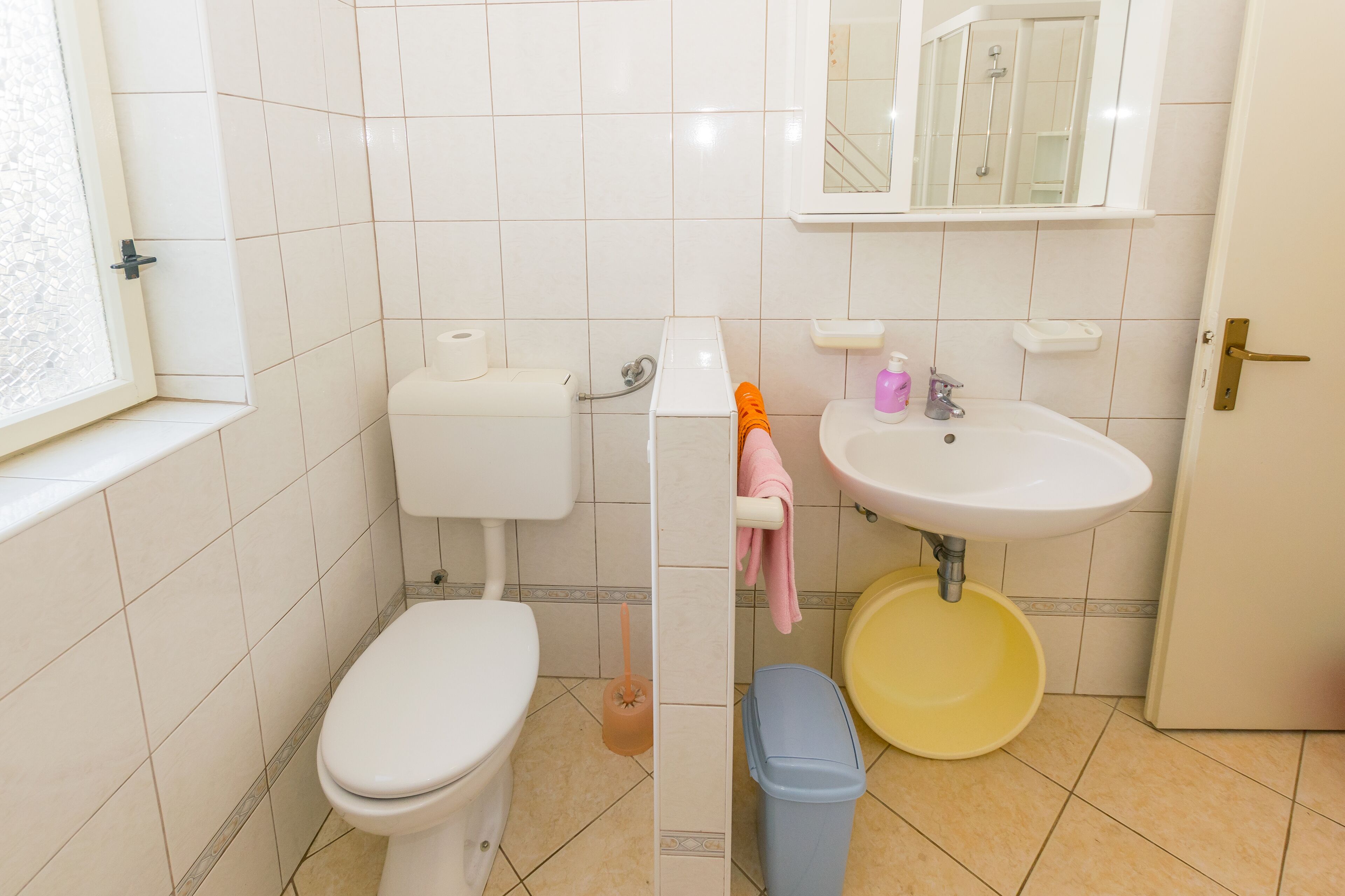 A bathroom with a toilet, sink, and a trash bin.
