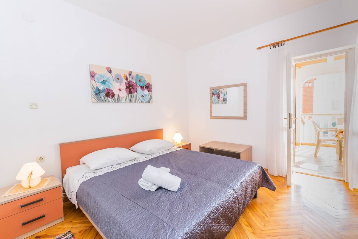 A bedroom with a bed, bedside tables, a nightstand, a mirror, and a door leading to a balcony.