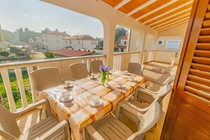 A covered outdoor dining area with a checkered tablecloth, white chairs, and a view of the surrounding buildings. - Apartments Grakalic great location (Medulin)