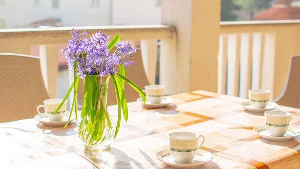 Un balcón con una mesa dispuesta para tomar té, con un jarrón de flores y varias tazas.
