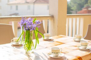 A balcony with a table set for tea, featuring a vase of flowers and several teacups. - Apartments Grakalic great location (Medulin)
