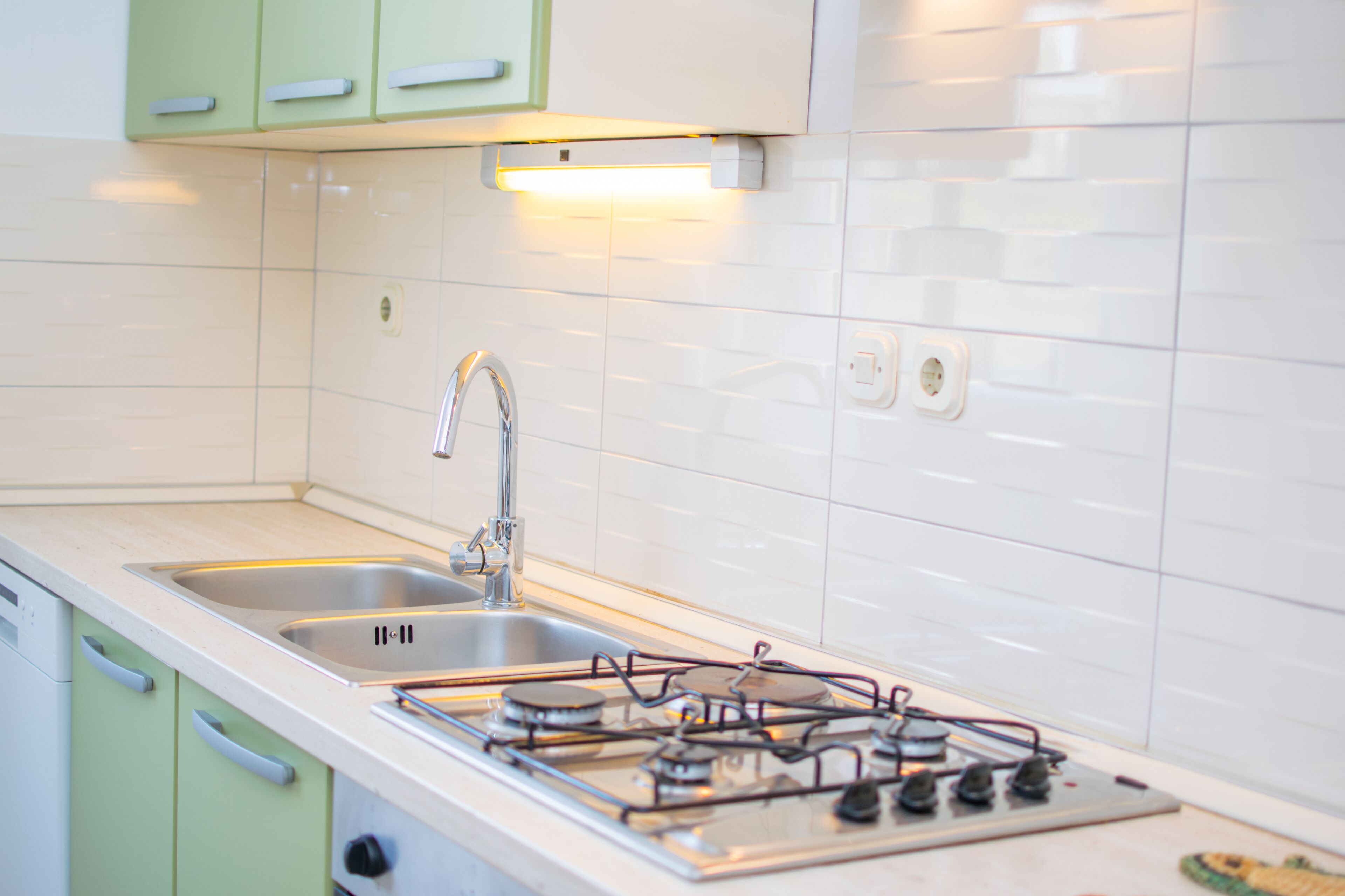 A kitchen with a stainless steel sink, a gas stove, and green cabinets.
