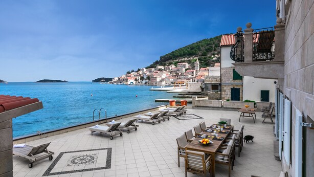 Una terrazza con poltrone relax, un tavolo da pranzo e vista sul mare e su una cittadina costiera.