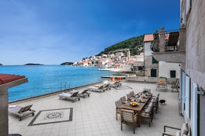 Una terraza con sillones, una mesa de comedor y vistas al mar y a un pueblo costero.