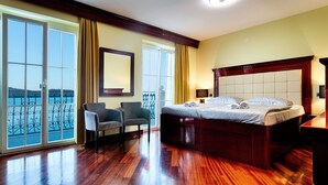 Una camera d'albergo con un letto grande, una sedia, una scrivania e vista sul mare attraverso ampie finestre.