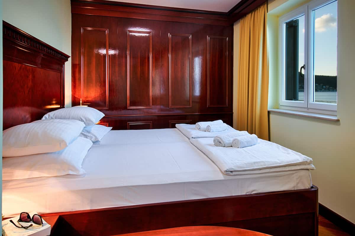 A hotel room with a large bed, wooden headboard, and a window with curtains.