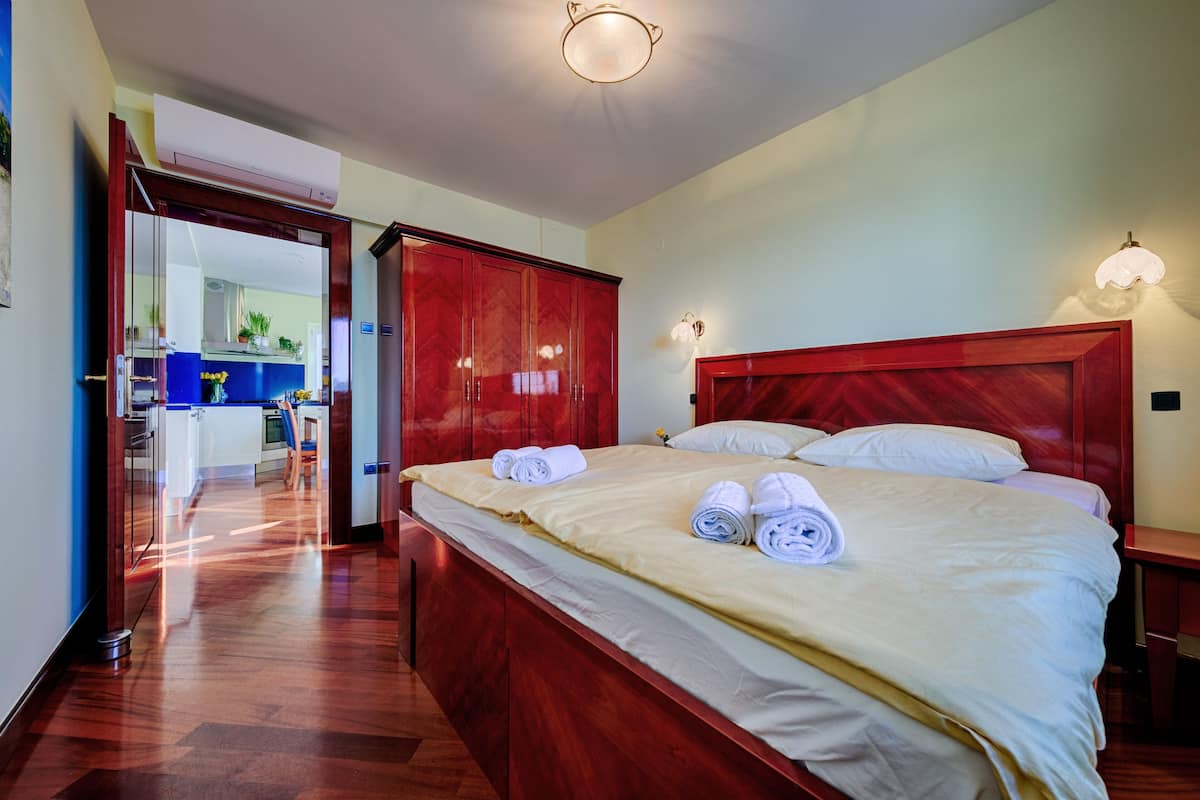 A hotel room with a wooden bed, a red wardrobe, and a kitchenette in the background.