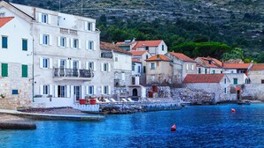Una cittadina costiera con edifici lungo il lungomare, un mare blu limpido e boe rosse.