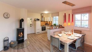 A modern kitchen with a central island, a dining area with a glass table, and a wood-burning stove.