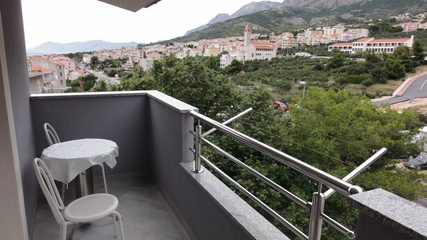 Un balcon avec une table et une chaise, donnant sur une ville avec des bâtiments et des montagnes en arrière-plan.