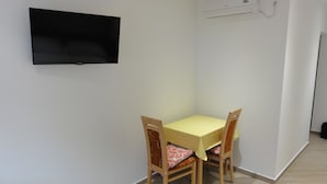 Un petit coin repas avec une table et des chaises, un téléviseur à écran plat fixé au mur et un appareil de climatisation.