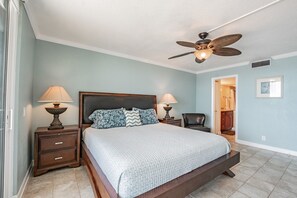 A bedroom with a bed, two bedside tables with lamps, a ceiling fan, and a door leading to a bathroom.