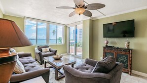 Uma sala de estar com ventilador de teto, televisão e vista para o exterior.