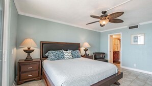 Quarto com cama, duas mesas de cabeceira, ventilador de teto e porta para outro cômodo.