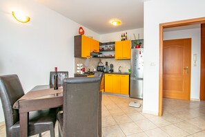 A modern kitchen with yellow cabinets, a dining table with chairs, and a wooden door. - Apartment Keti (Porec)