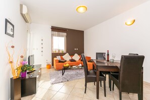 A modern living room with a sofa, dining table, chairs, and a TV. - Apartment Keti (Porec)