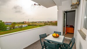 Un balcón con una mesa y sillas, un frutero y vistas a casas y vegetación.