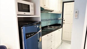 A compact kitchen with a microwave, a blue refrigerator, a sink, and white cabinets. - Floor 12 Jomtien Beach Condo (Pattaya)