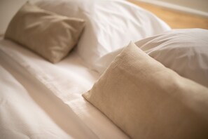 Ein Bett mit weißer Bettwäsche und beigen Kissen.