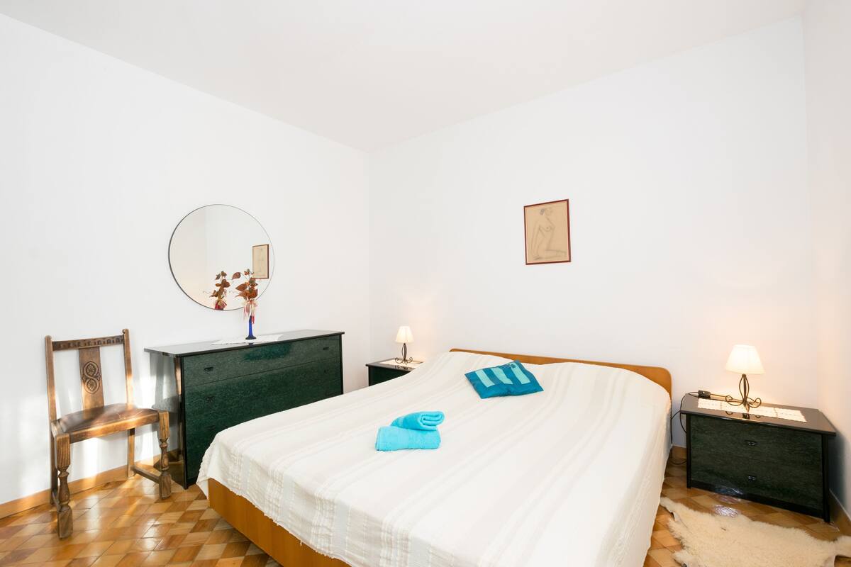 A neatly arranged bedroom with a bed, a dresser, a chair, and a nightstand with lamps.