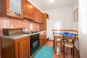 A compact kitchen with wooden cabinets, a built-in oven, a sink, and a dining area with a table and chairs. - Apartments Mirjana (Pula)
