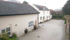 A residential area with houses, a gravel driveway, and a small garden area with potted plants. - Vale View Cottages - The Stables Cottage 5 Star. Near beach & town, Pets welcome (Prestatyn)