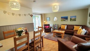 A cozy living room with a brown leather sofa, wooden chairs, a coffee table, and a dining table with a patterned tablecloth. - Vale View Cottages - The Stables Cottage 5 Star. Near beach & town, Pets welcome (Prestatyn)