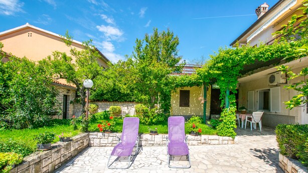 Ein Innenhof mit zwei violetten Liegestühlen, einem Steinboden und einem kleinen Gartenbereich mit Blumentöpfen und einer Laterne.
