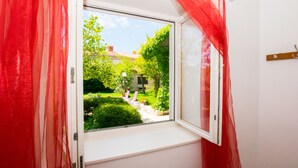 Ein Fenster mit roten Vorhängen, Blick auf einen Garten und ein Holz-Kleiderständer.