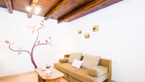 Ein gemütliches Wohnzimmer mit Holzboden, einem beigefarbenen Sofa, einem kleinen Holztisch und einer Wandmalerei eines Baumes.