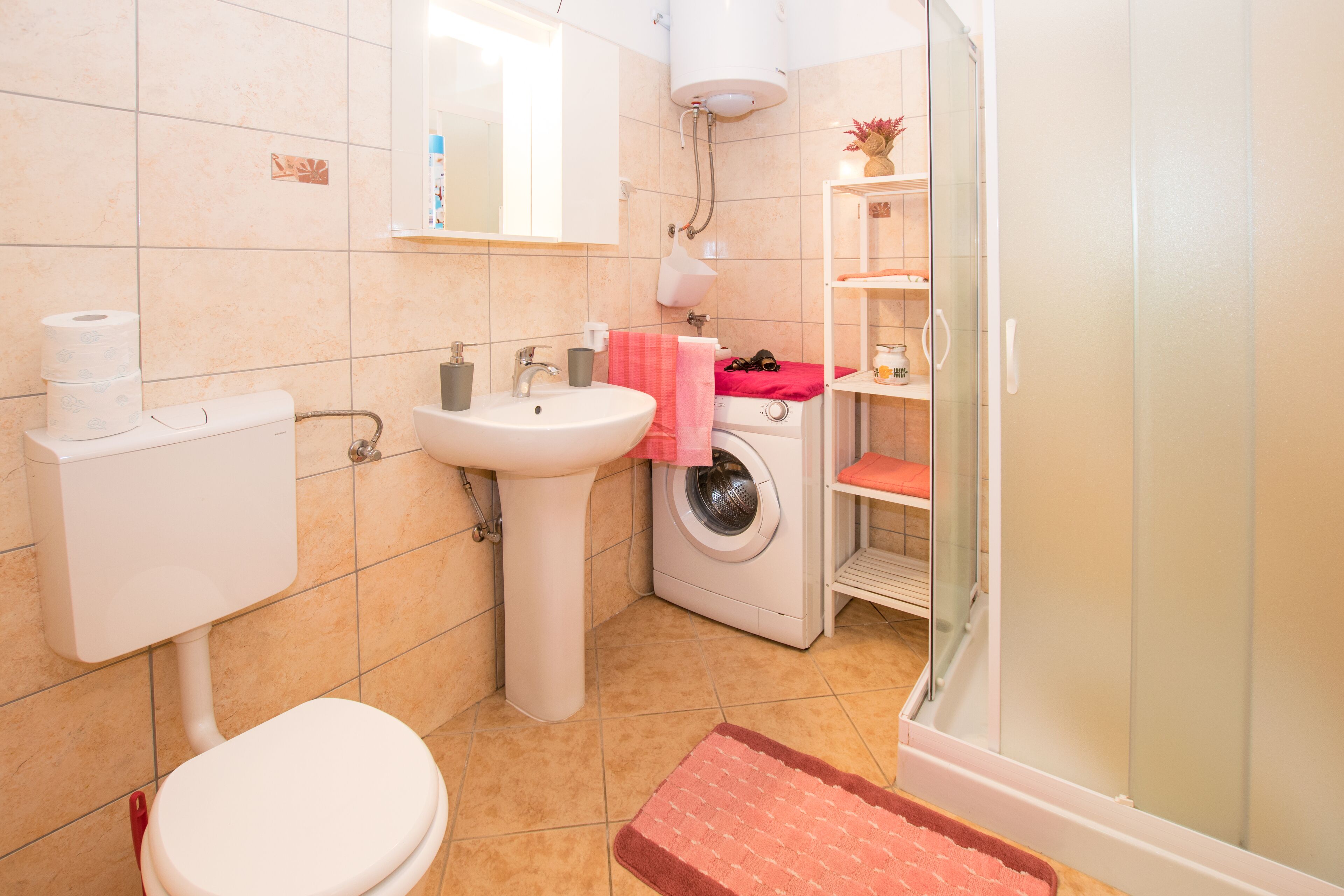 A bathroom with a toilet, sink, washing machine, and a glass shower enclosure.